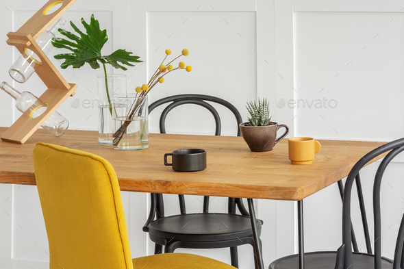 Stylish yellow chair at wooden dining table in trendy interior .